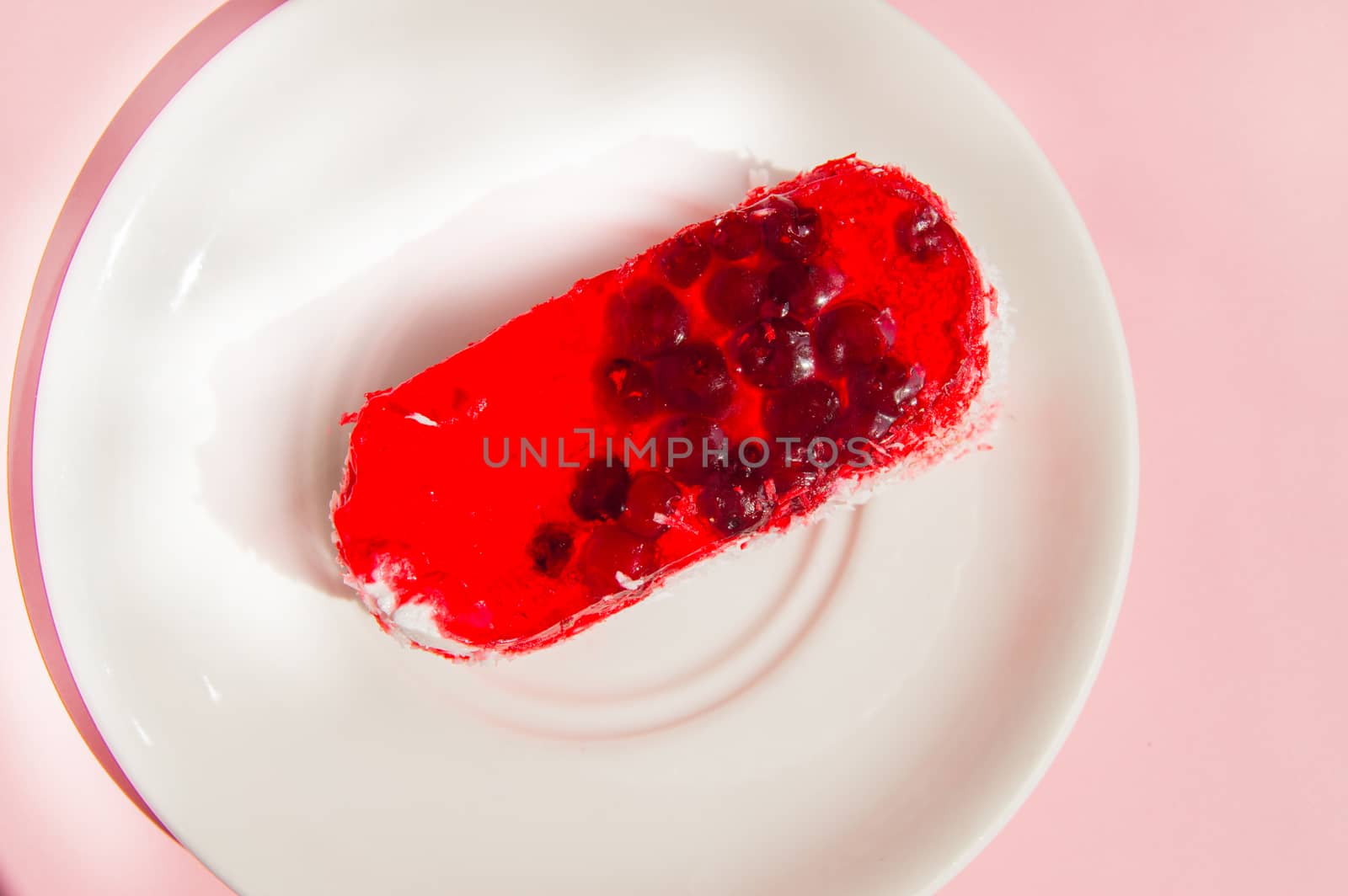 Exquisite souffle cake with lingonberry jelly, with berry glaze and coconut on a white plate, top view close-up, pink background.