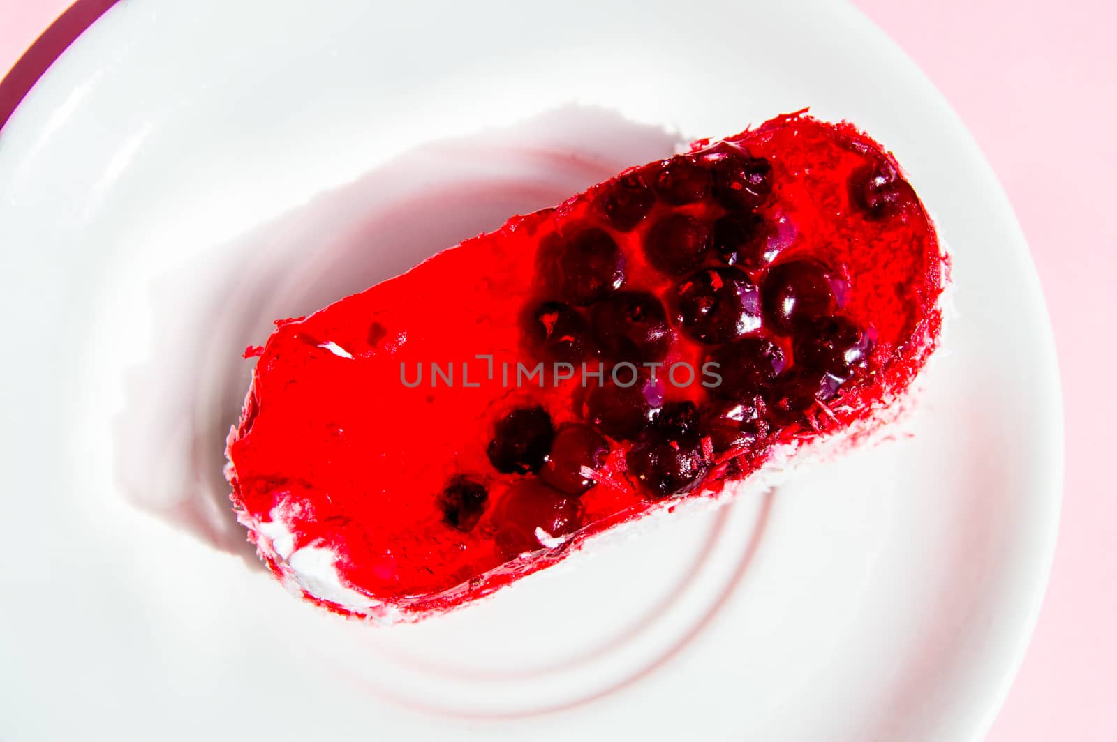 Exquisite souffle cake with lingonberry jelly, with berry glaze and coconut on a white plate, top view close-up, pink background.