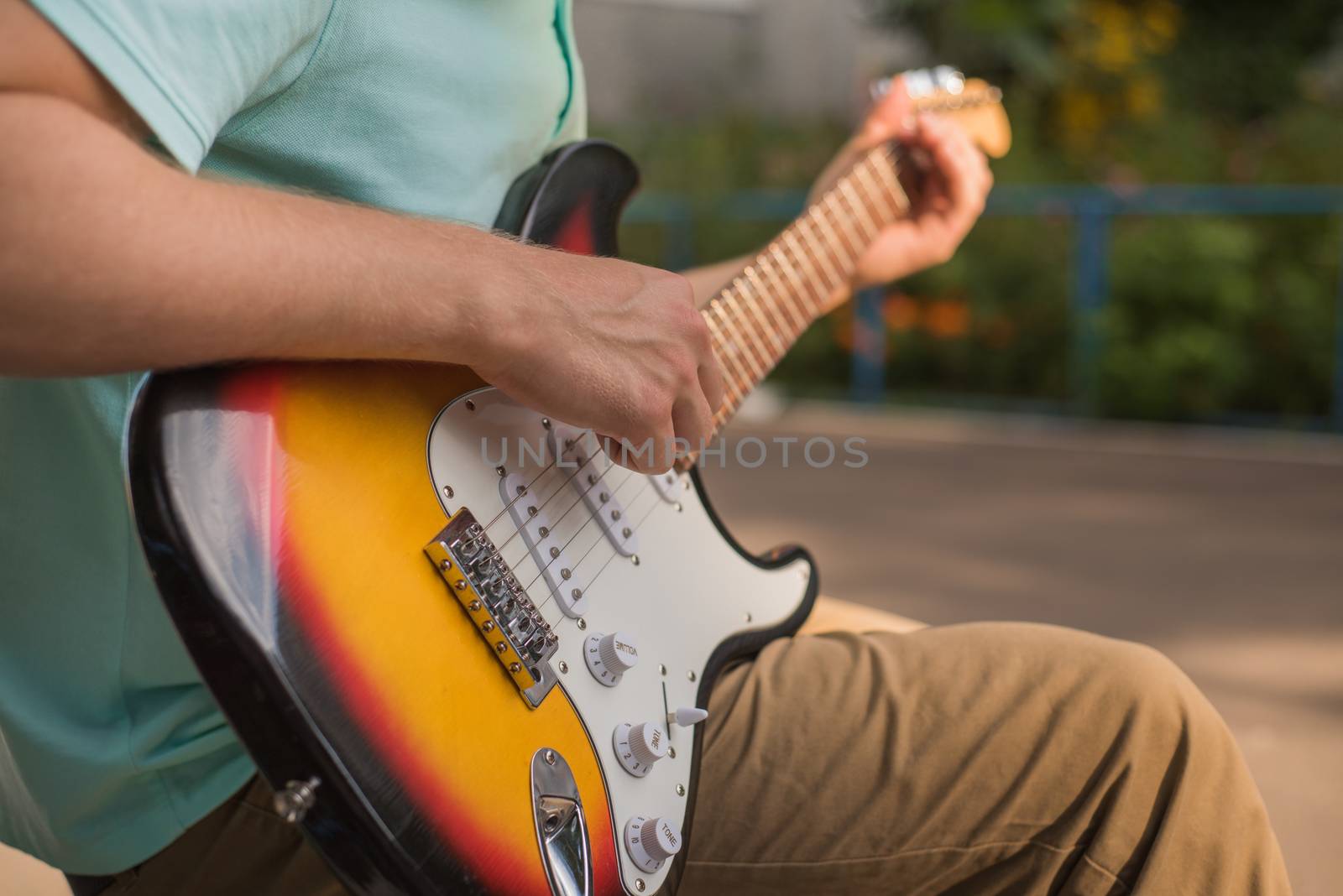 Young man hipster sitting playing guitar, close-up.