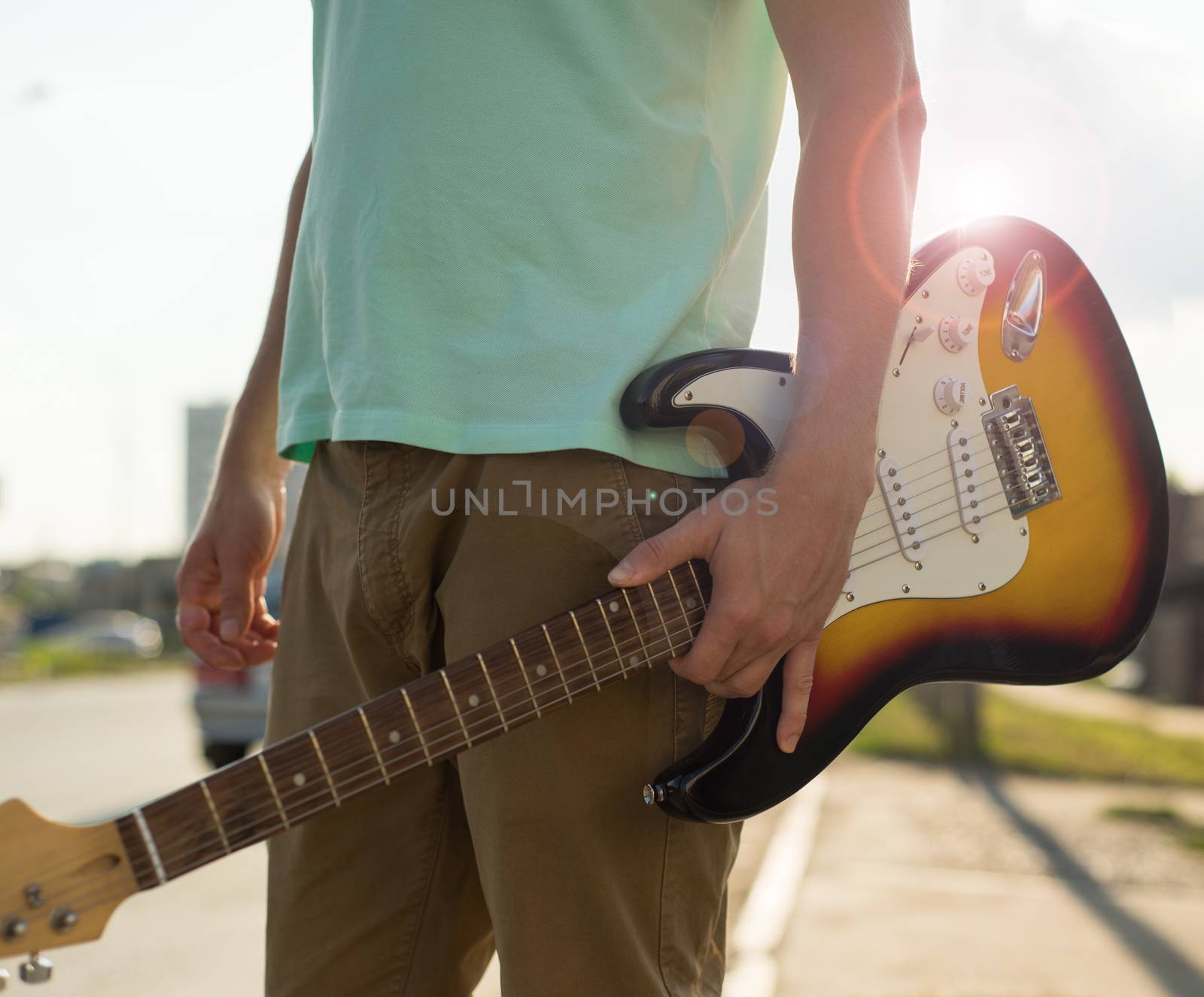Young man hipster with a guitar stands on the road in the sunlight.