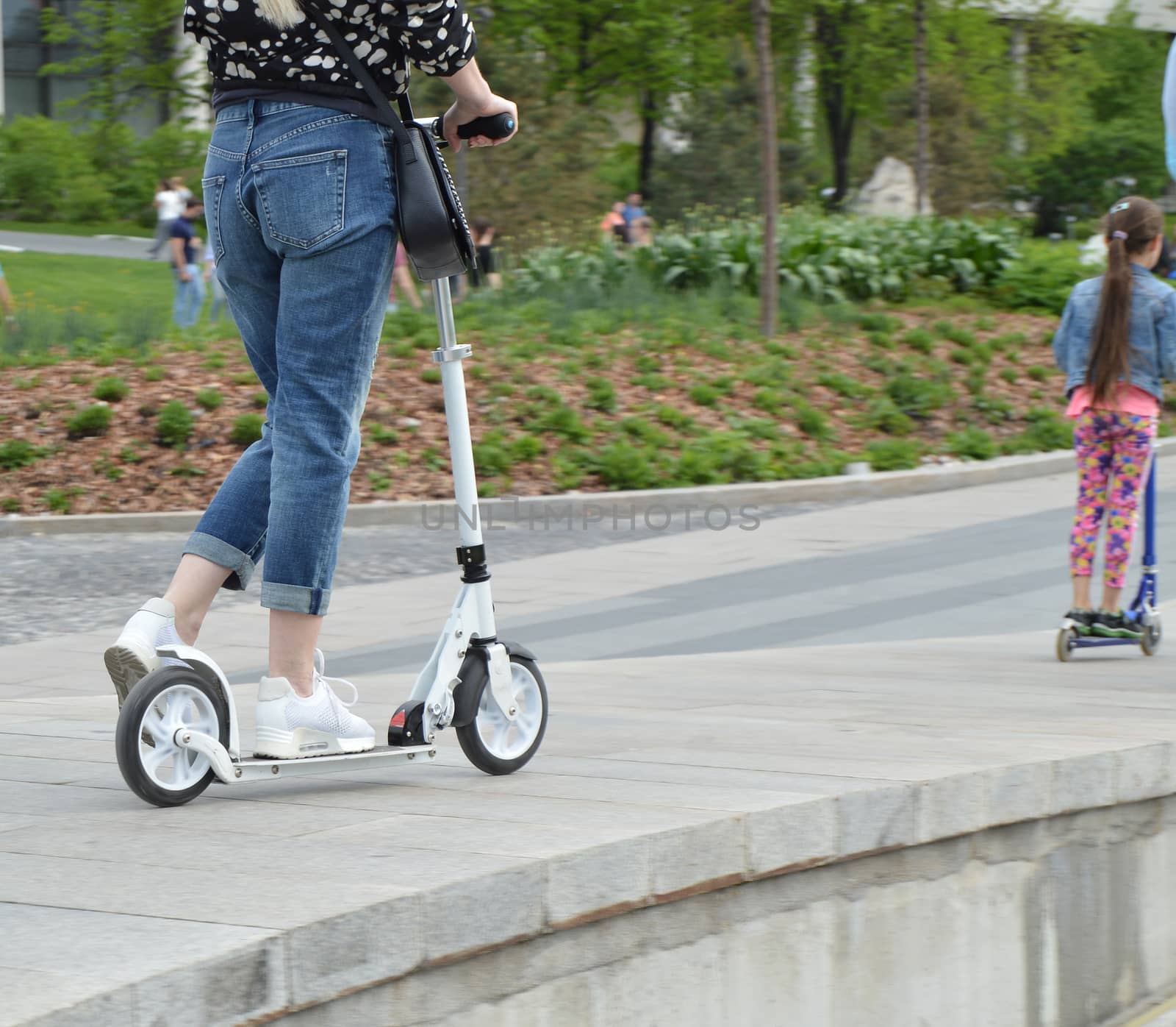 woman and her daughter ride together outdoors in the Park on the scooter.