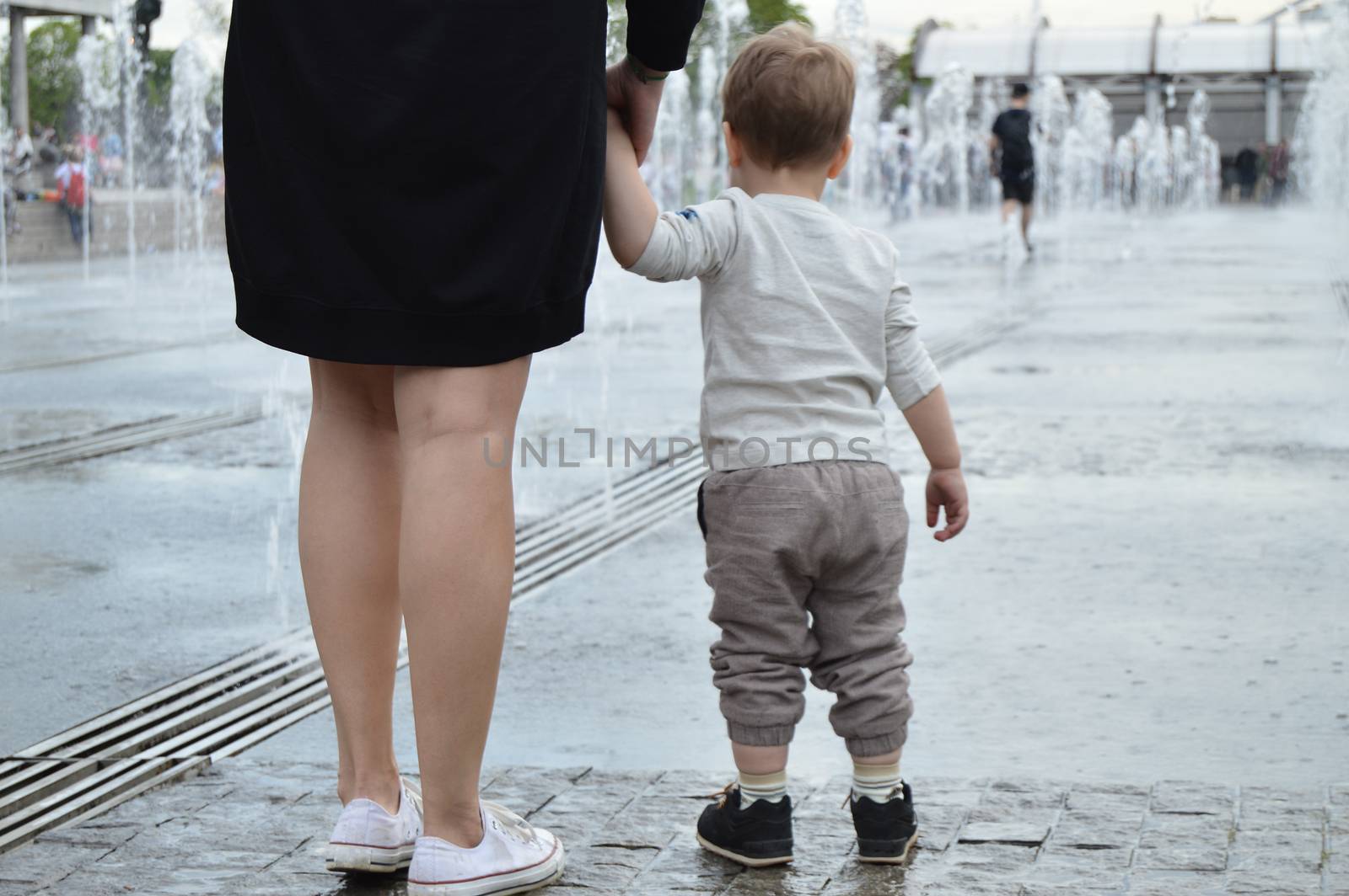 Mother and child standing together holding hands in a summer Park, look at the fountain. The view from the back. The concept of unity and care by claire_lucia