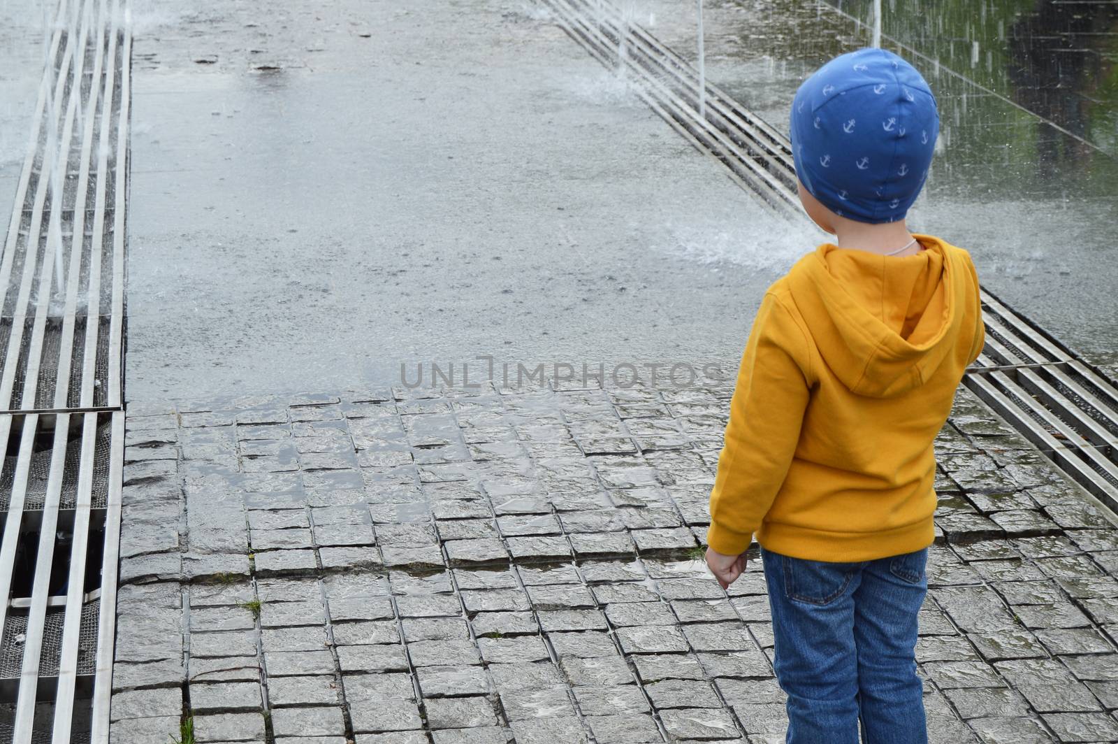 child standing near a puddle in the Park near the fountain, watching the water jets by claire_lucia
