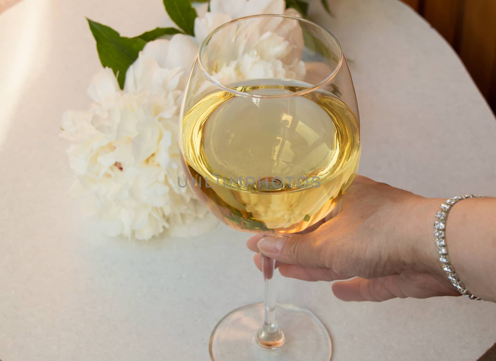 glass of white wine holding woman's hand in the bracelet. Closeup