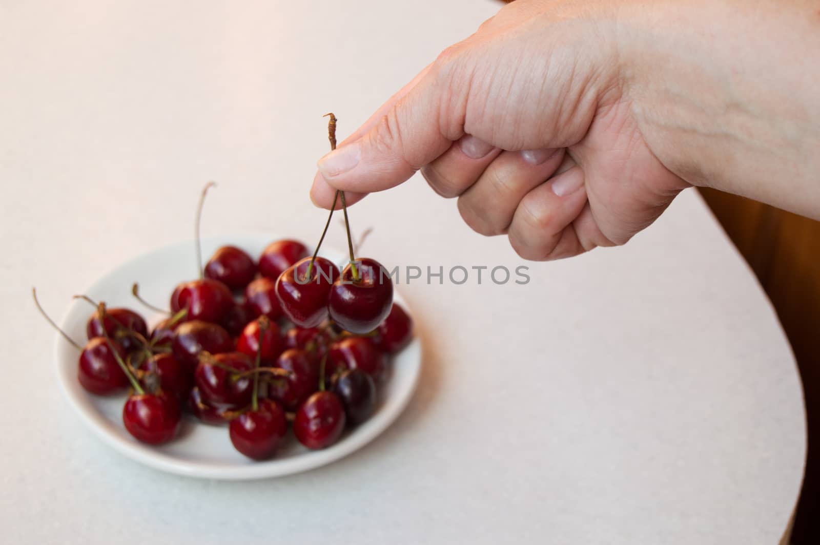 Ripe cherry in the hand and on a white plate, selective focus on hand.