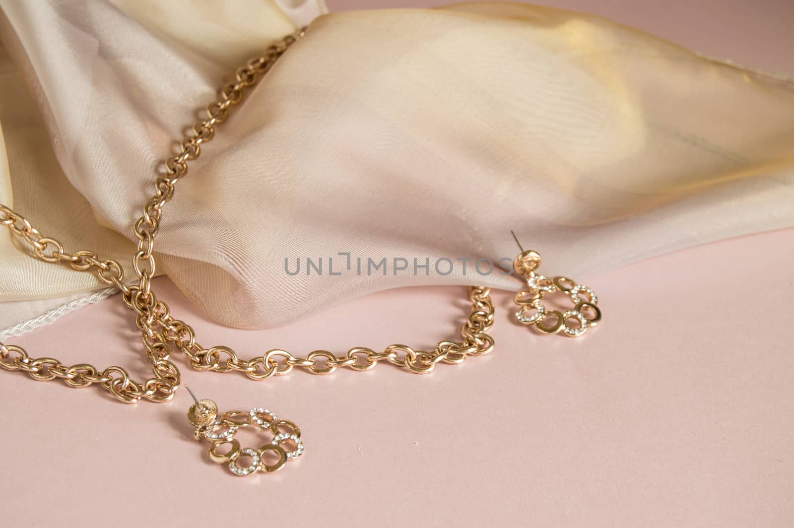 Luxury gold jewelry chain and earrings on pink background with silk, copy space, selective focus by claire_lucia