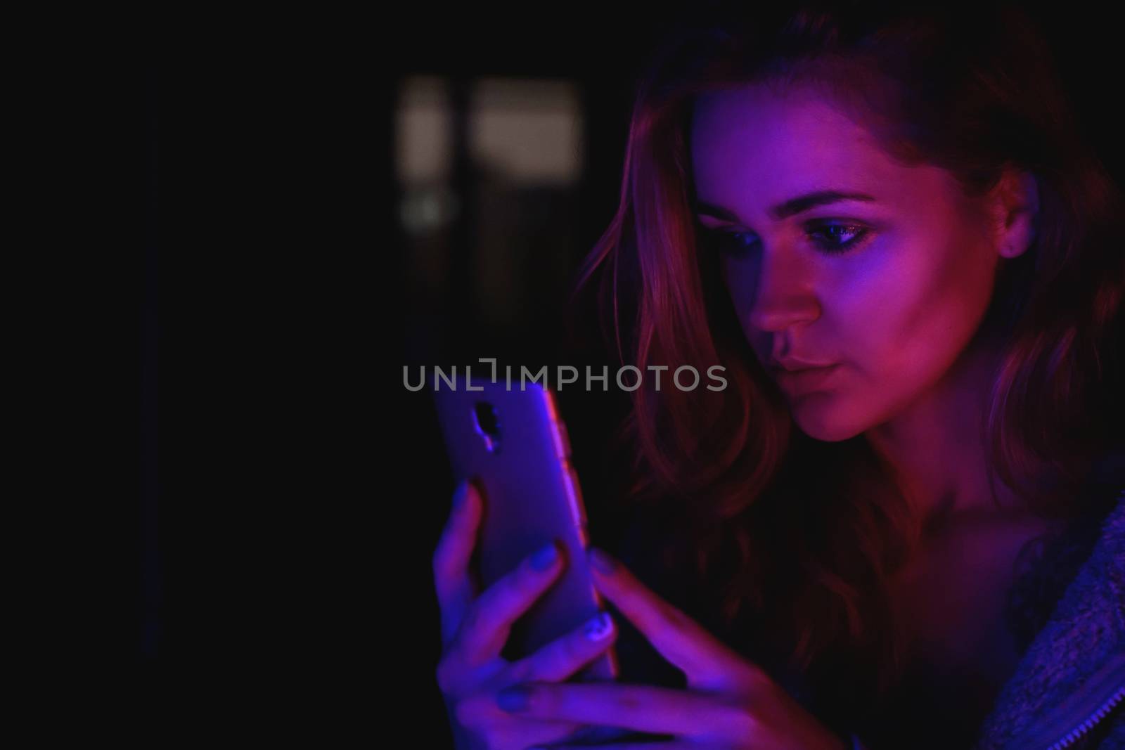 Girl using cellphone at night with neon light - pink and blue and black background