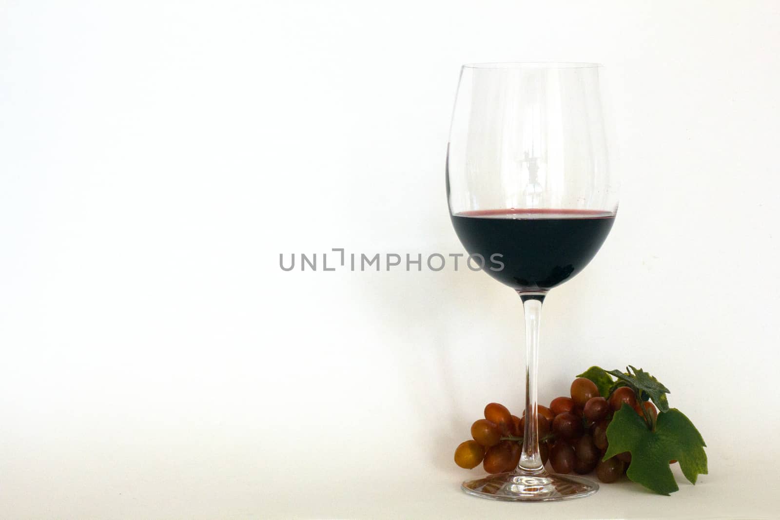 Glass of red wine with a bunch of grapes by Joanastockfoto