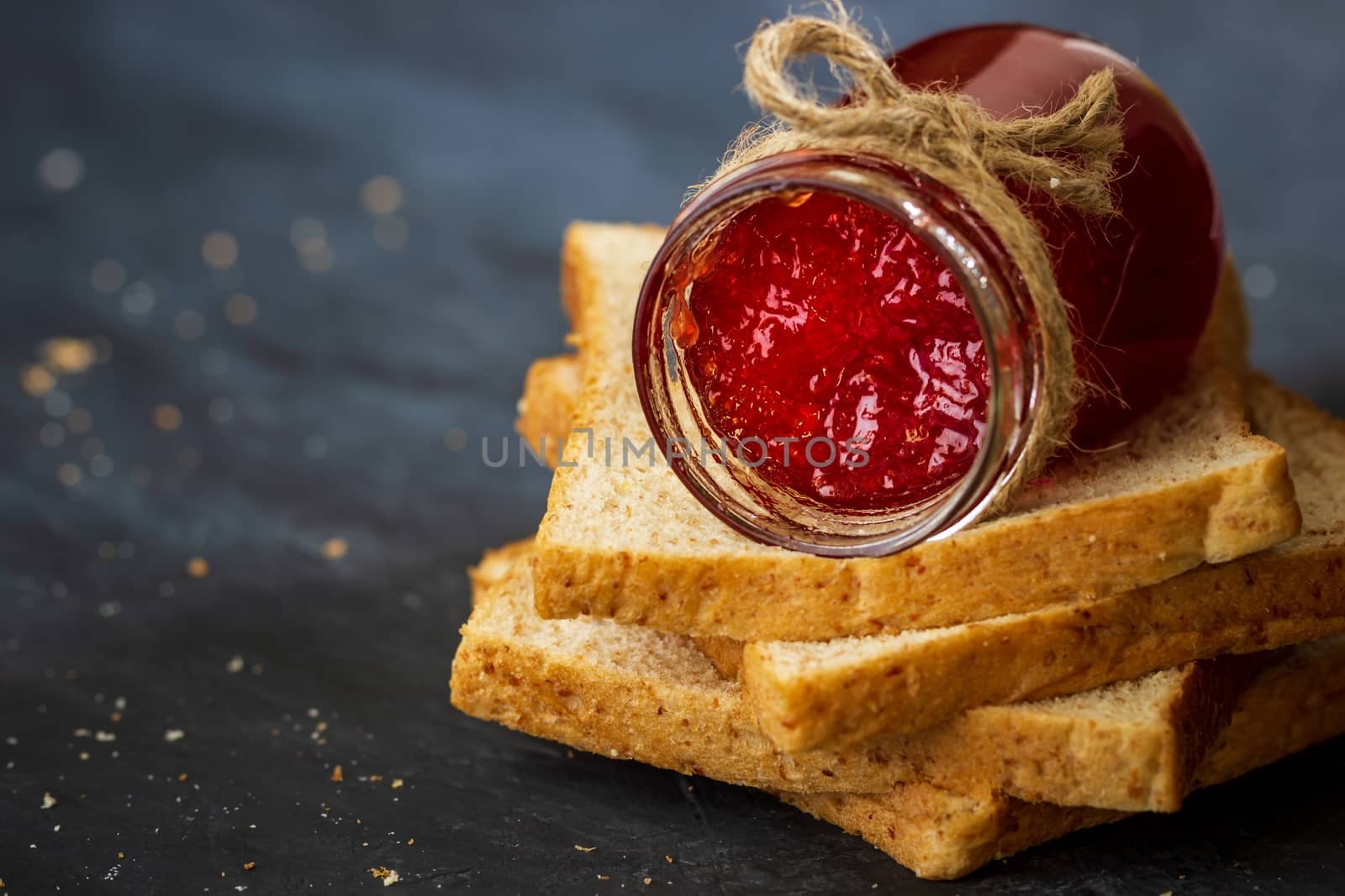 Strawberry jam bottle and whole wheat bread are stacked on a black background. Concept of breakfast and healthy food.