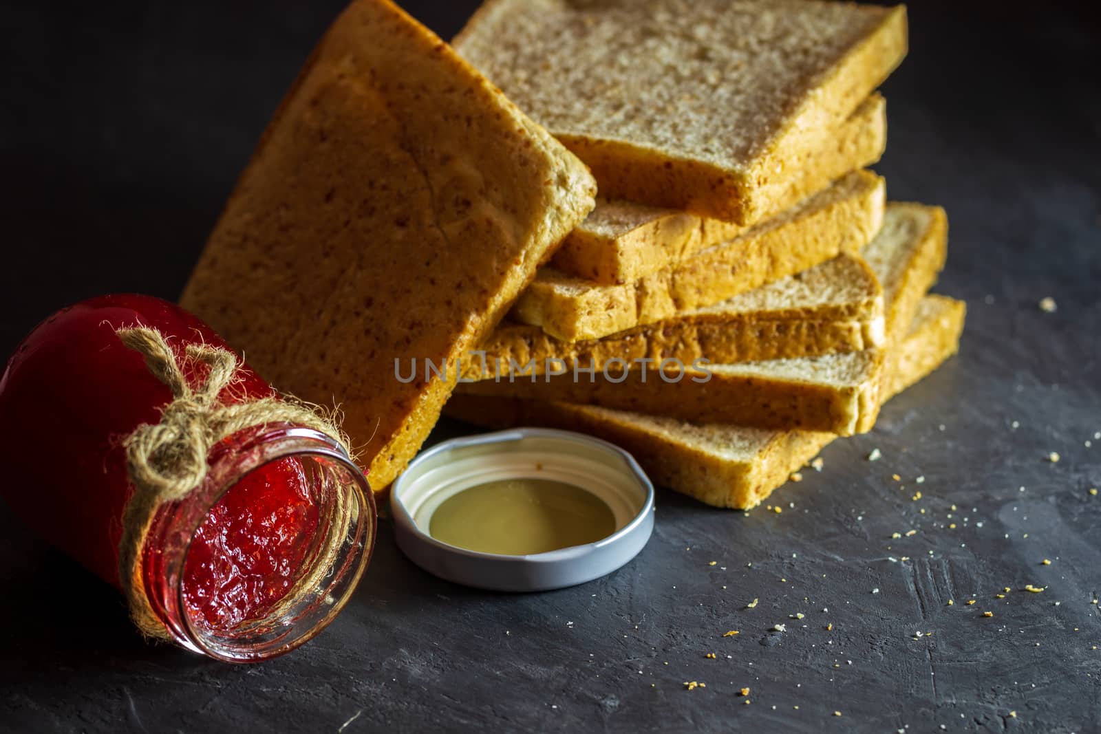 Strawberry jam bottle and whole wheat bread are stacked on a bla by SaitanSainam