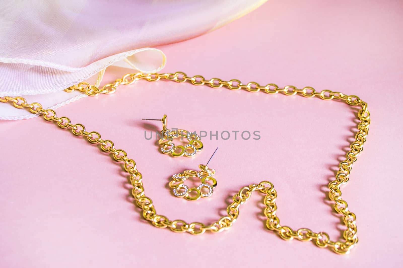 Luxury gold jewelry chain and earrings on pink background with silk, copy space, selective focus.