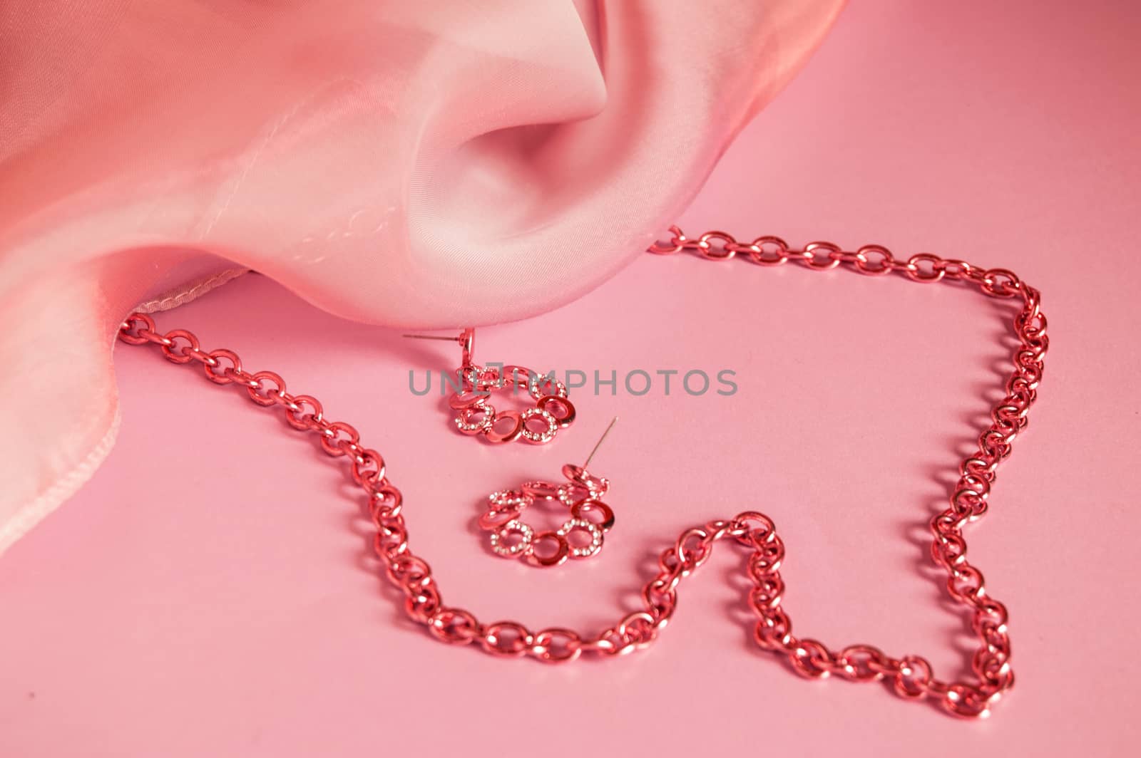 Luxury gold jewelry chain and earrings on coral background with silk, copy space, selective focus.