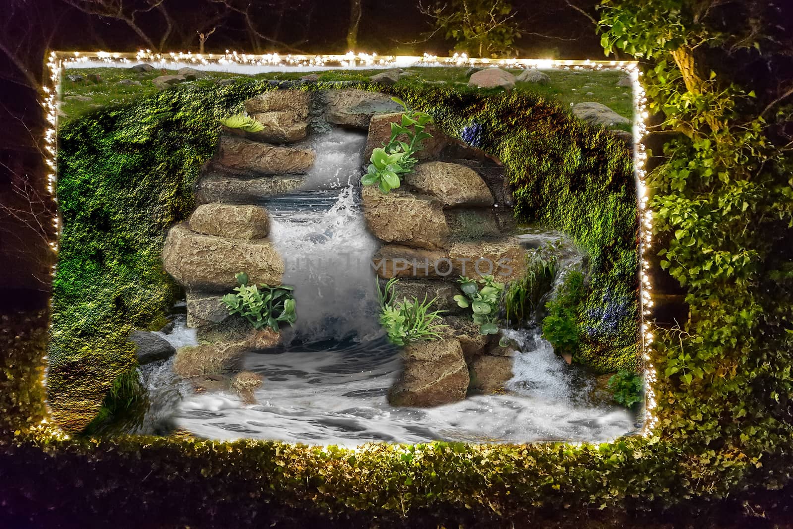 River water splashing on the rocks on billboard in a hedge edged with a string of lights.