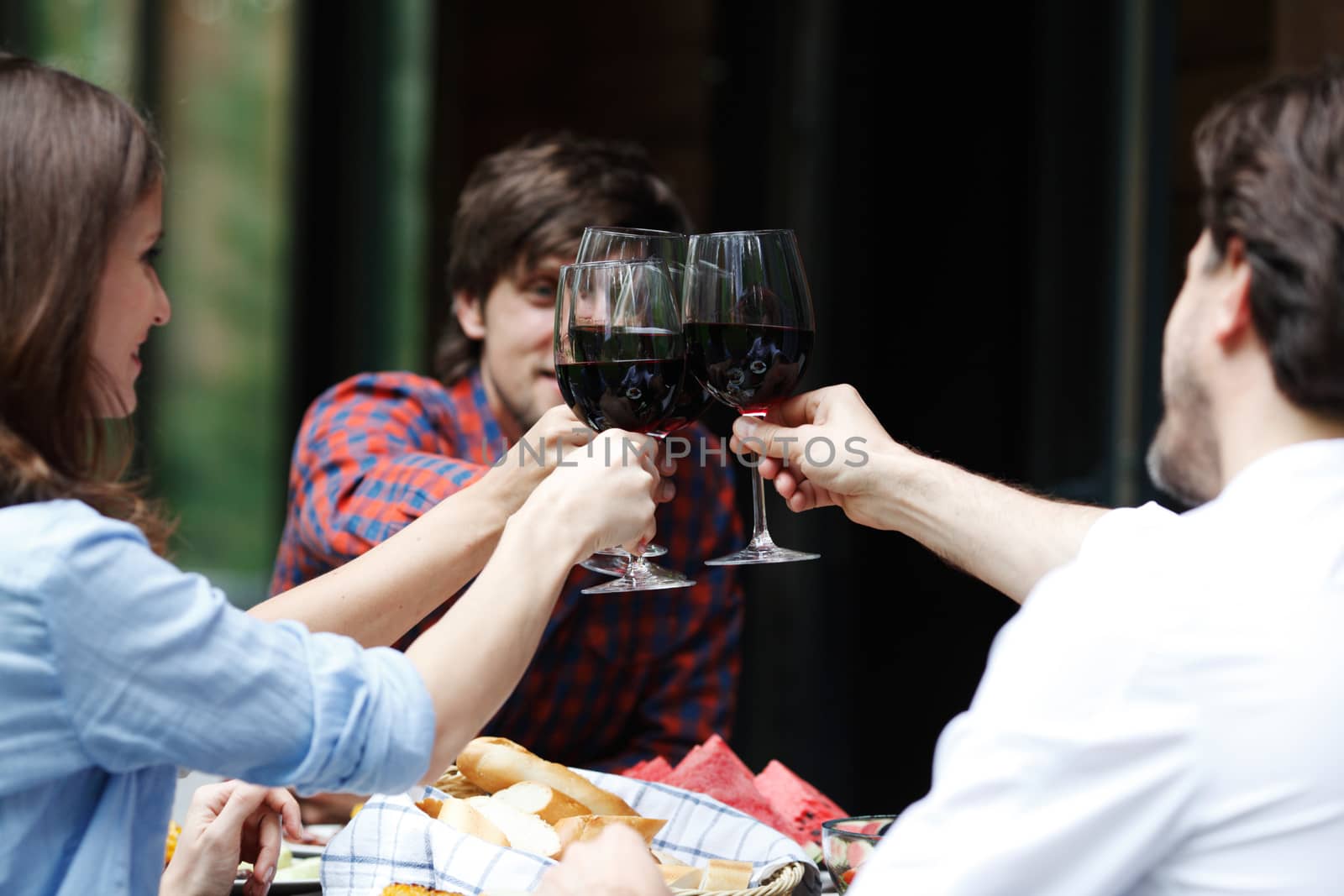 Friends clink glasses of red wine at outdoor dinner