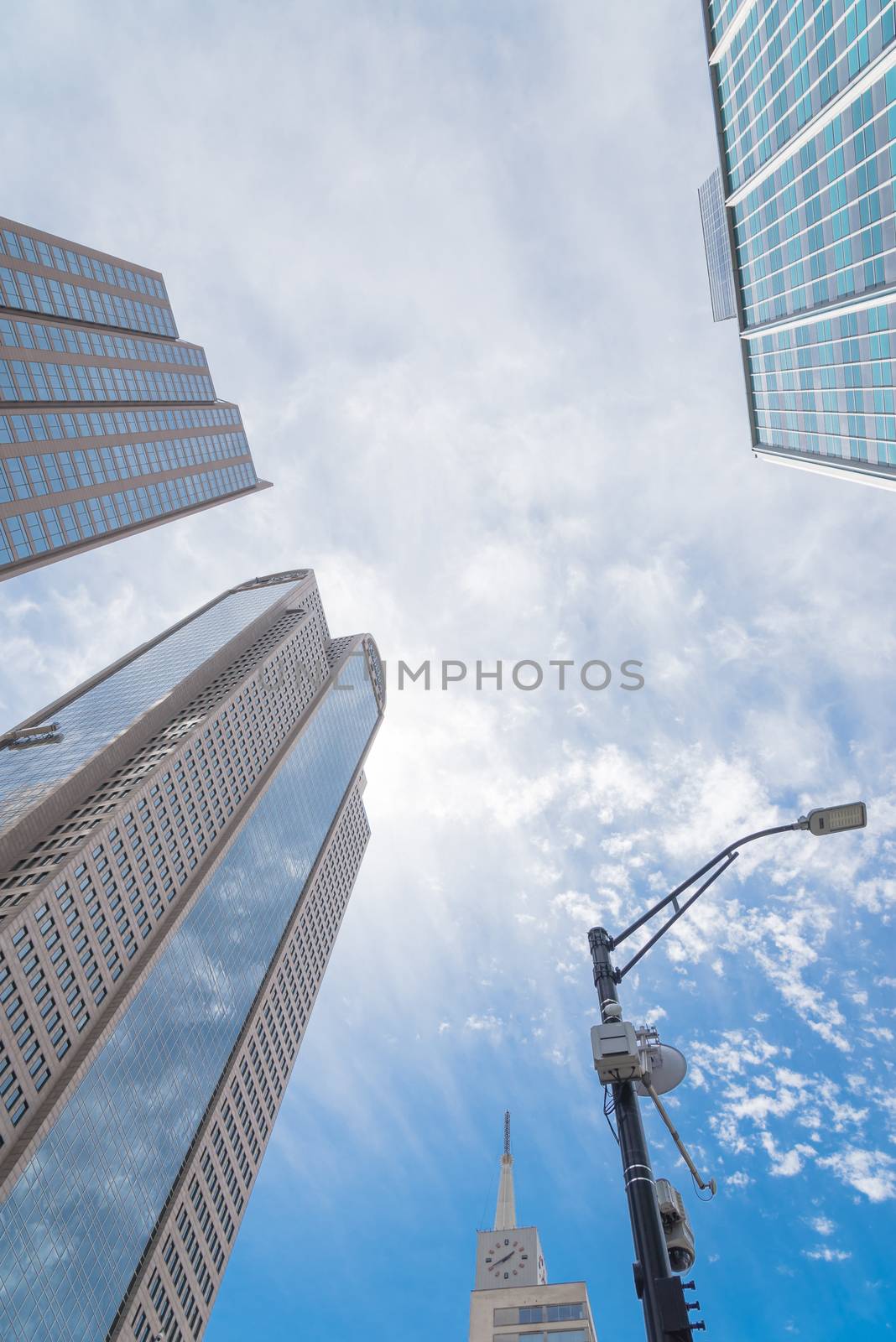 Lookup view of Dallas skylines and lamppost under cloud blue sky by trongnguyen