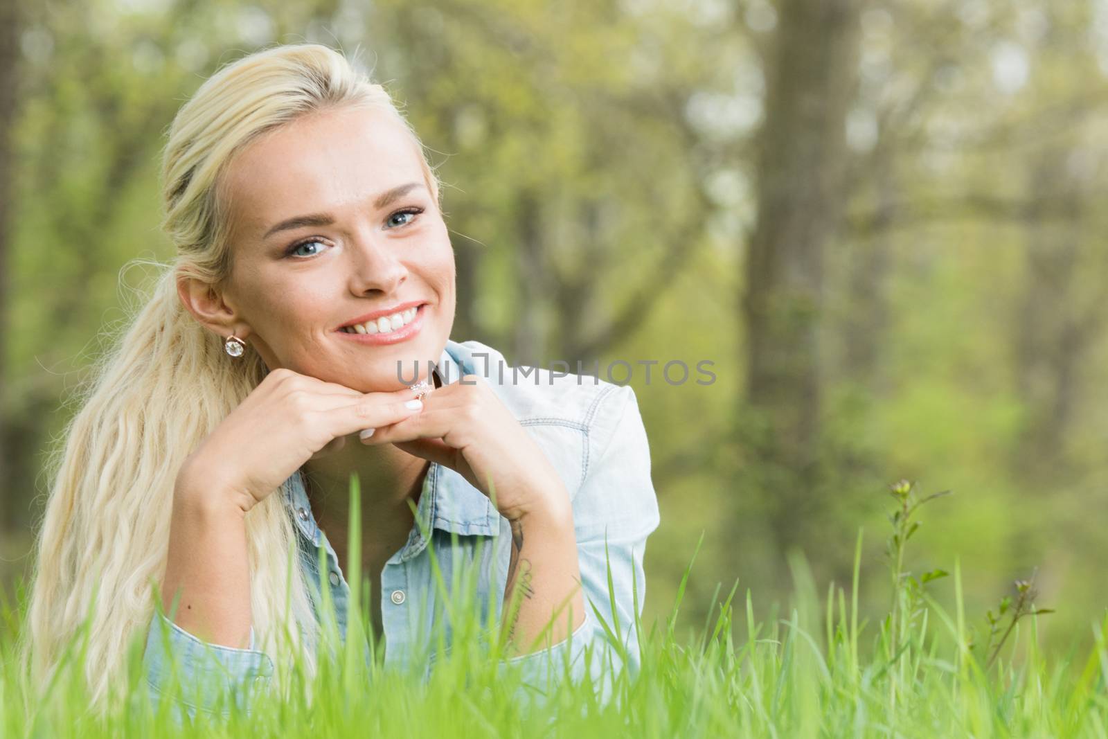 Blonde pretty girl laying on the grass in spring park and smiling