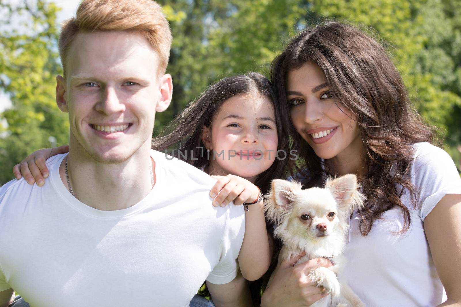 Happy smiling family of parents and daughter with pet dog in the park