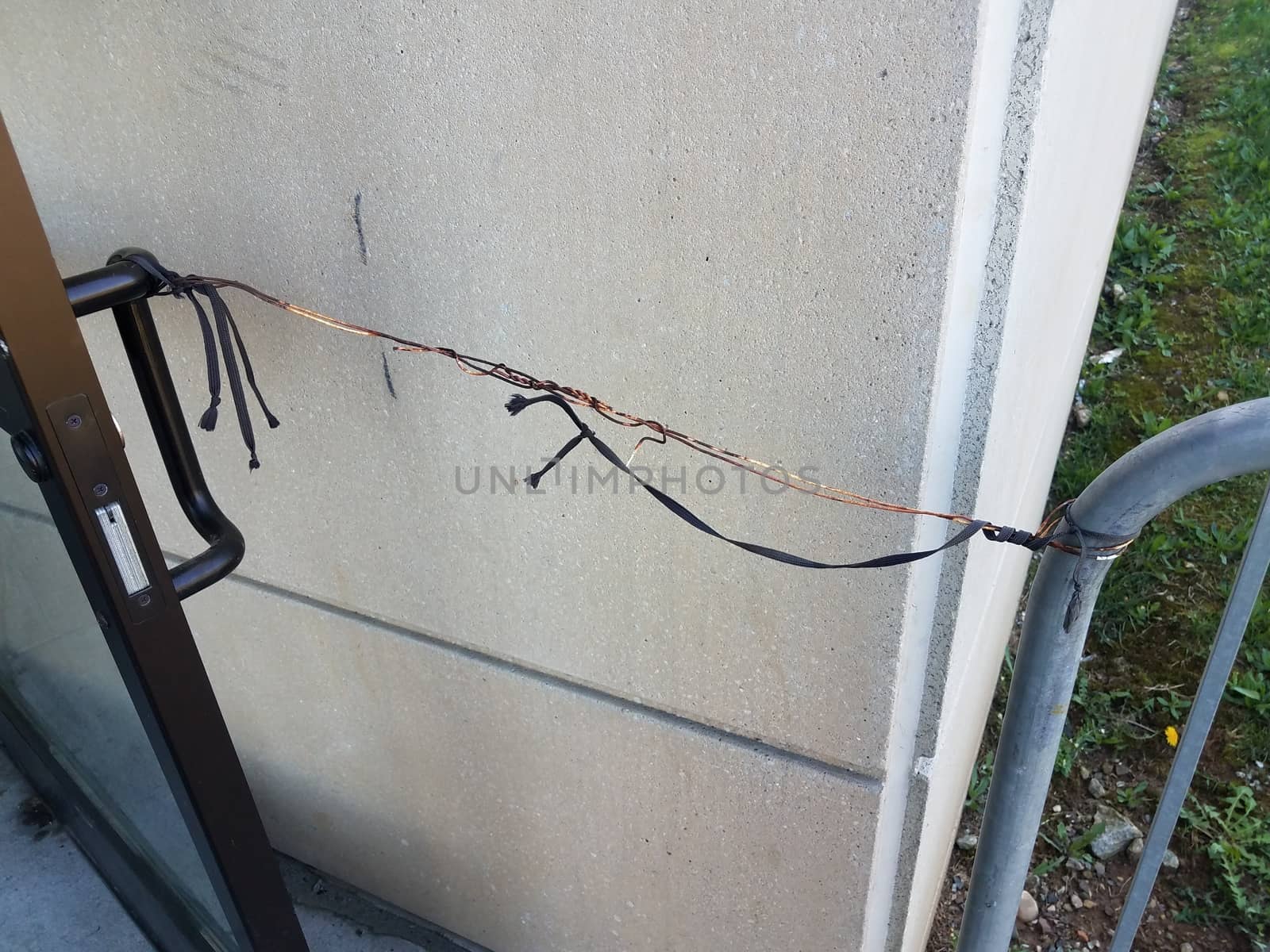 metal wire and string holding door open with metal fence and cement wall