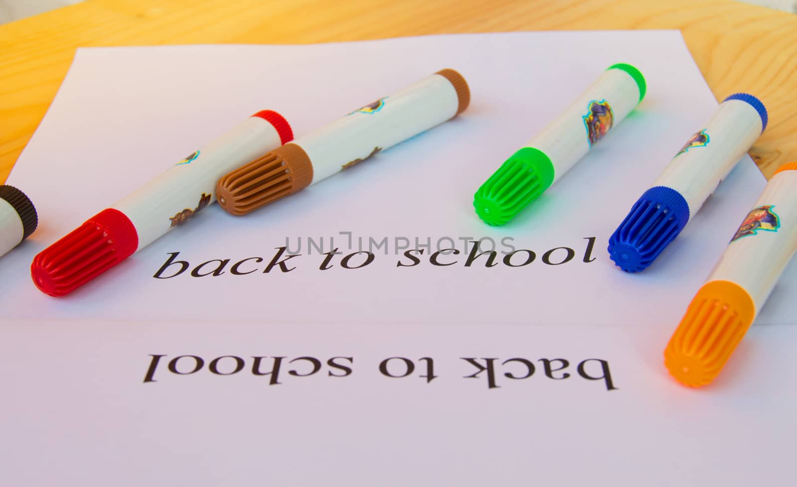 Back to school. A sheet of paper with text and colored markers on a wooden background, selective focus.