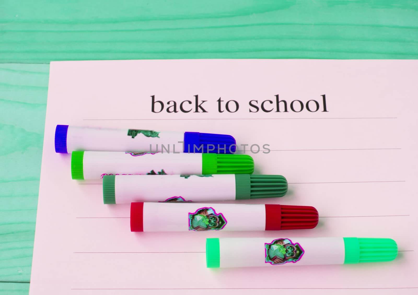 Back to school. Sheet of paper with text and colored markers on a green wooden background, top view.