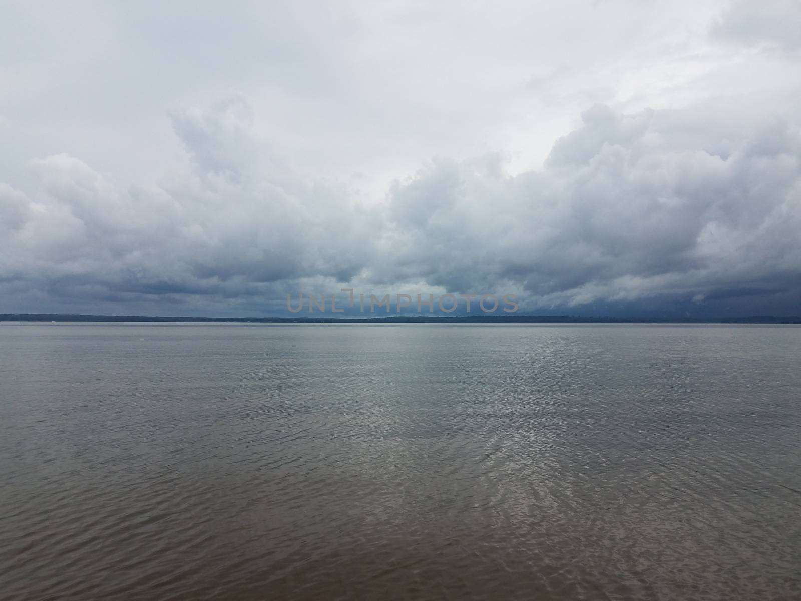 rain clouds forming over calm river near shore by stockphotofan1
