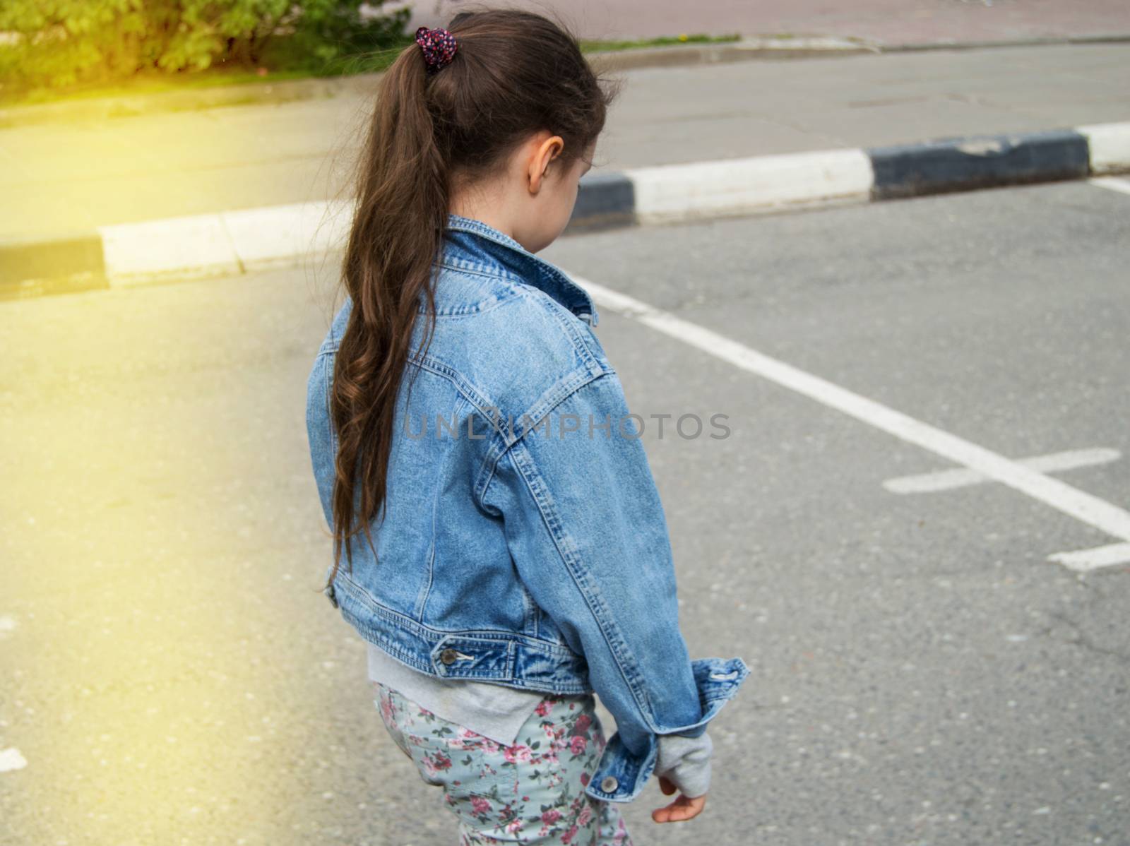 A sad little girl is walking along the road alone with her head down. The view from the back contrast with the sunlight by claire_lucia