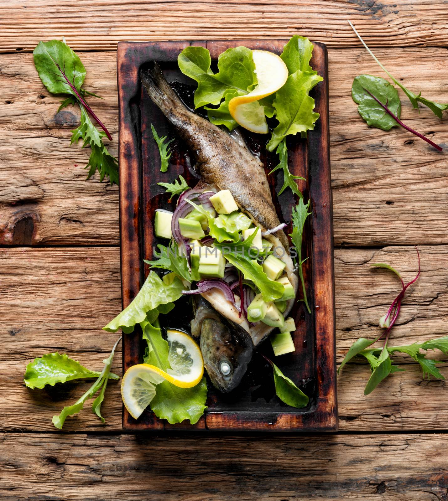 Baked trout with avocado on a wooden kitchen board.Baked fish with lettuce and avacado