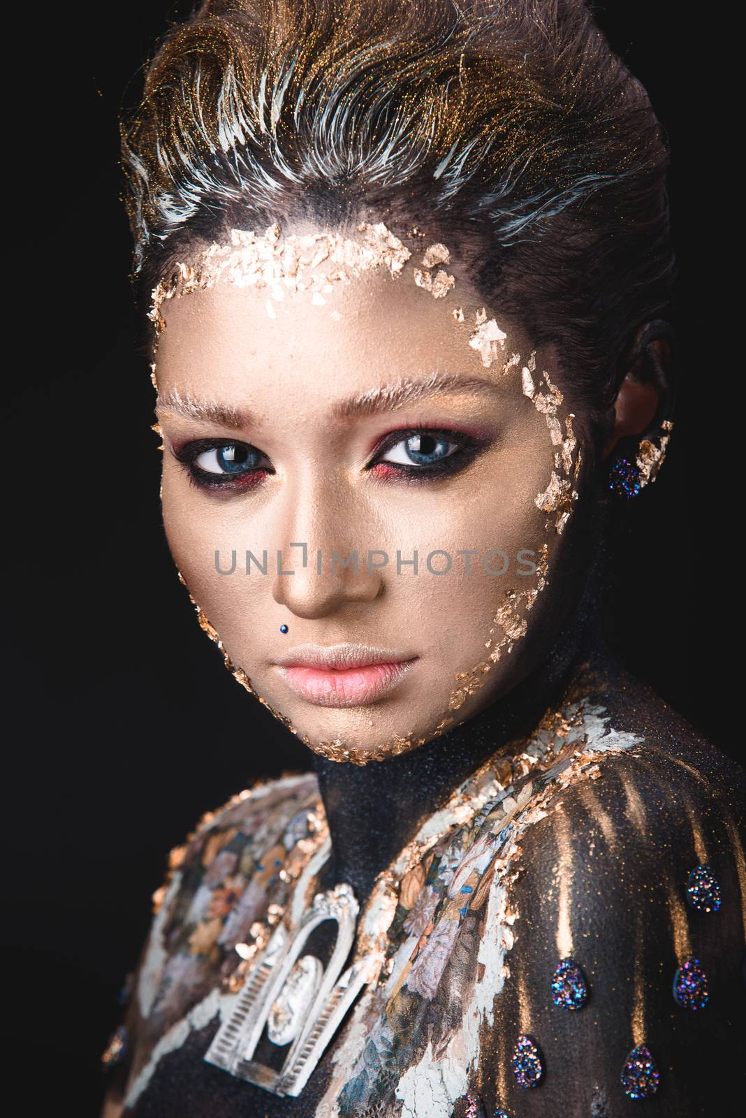 Portrait of a blue eyed young girl with creative golden makeup in the style of icon painting isolated on black background