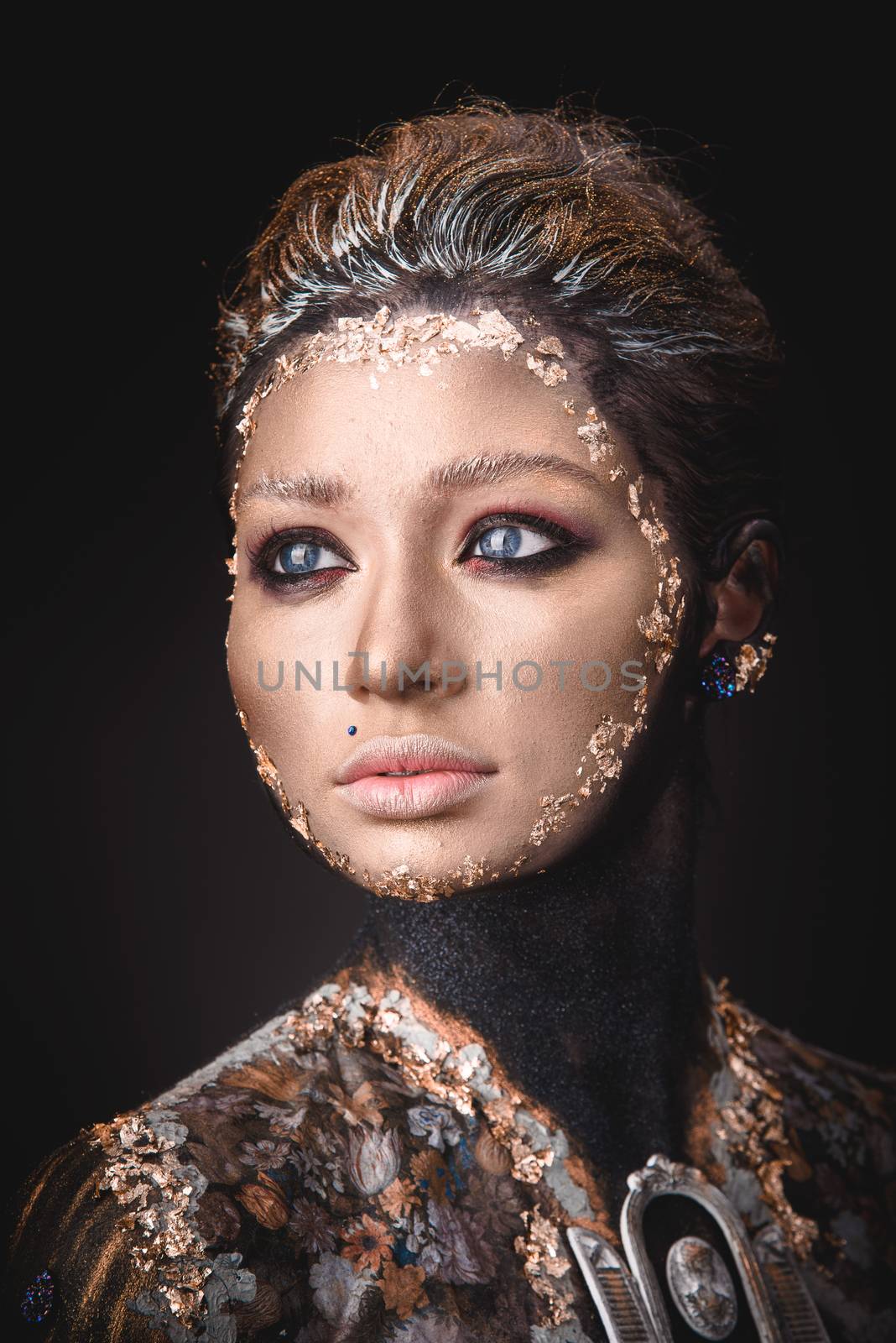 Portrait of a blue eyed young girl with creative golden makeup in the style of icon painting isolated on black background