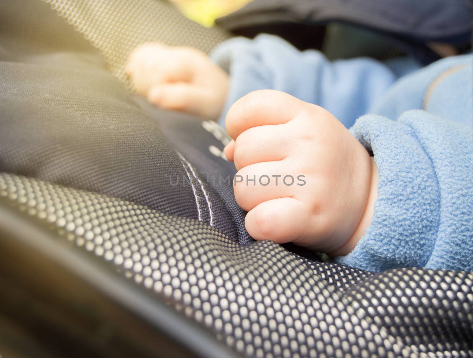 Child's hands fist, selective focus, the child is in the stroller while walking outdoors, close-up by claire_lucia
