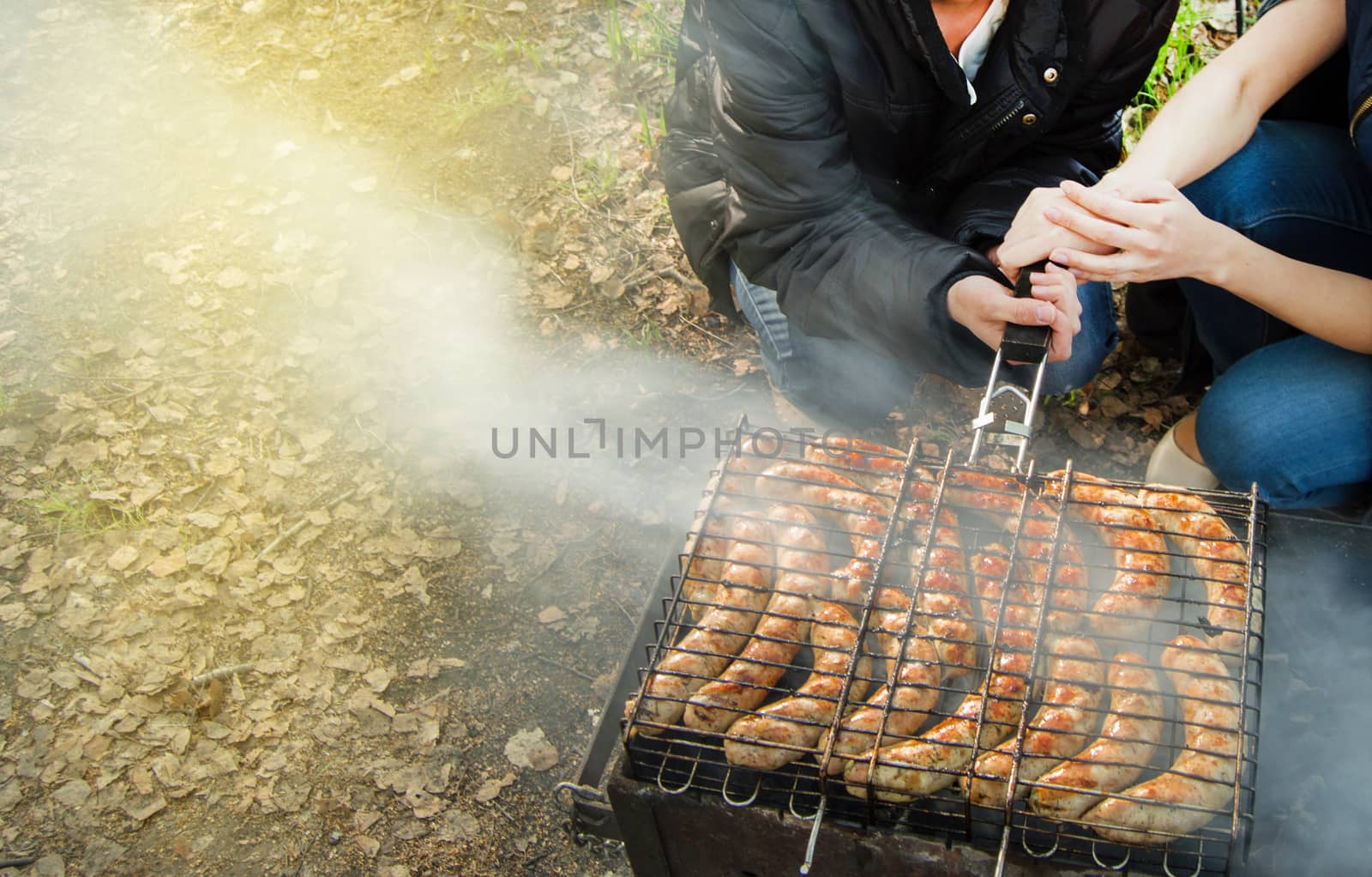 Summer, family, party. Picnic in nature with friends, the girls ' hands holding a metal lattice with fried sausages over the fire, copy the space by claire_lucia