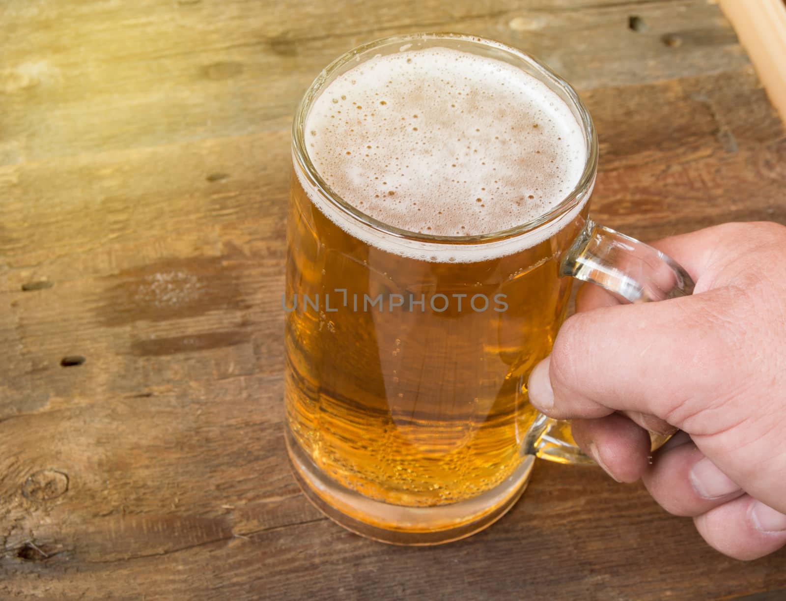 Summer, party, man's hand holding a mug of light beer on dark old wooden boards.