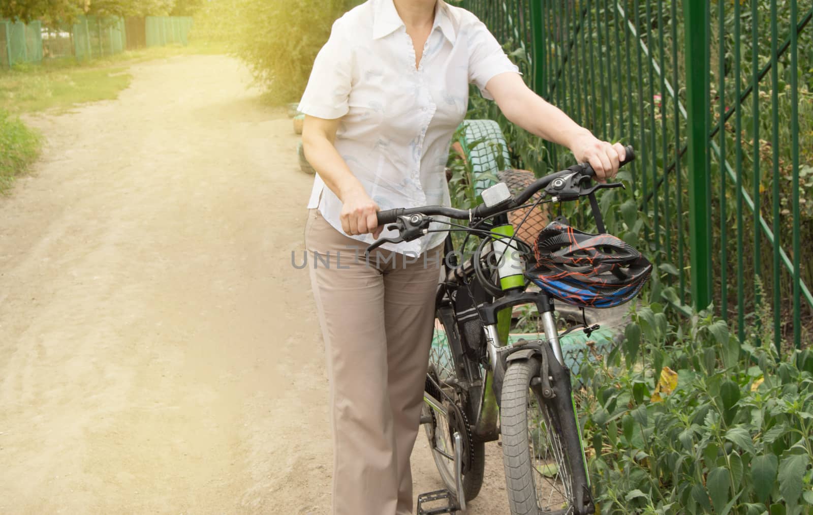Summer, family, happy young woman on a Bicycle standing on the road near the fence of the Park.