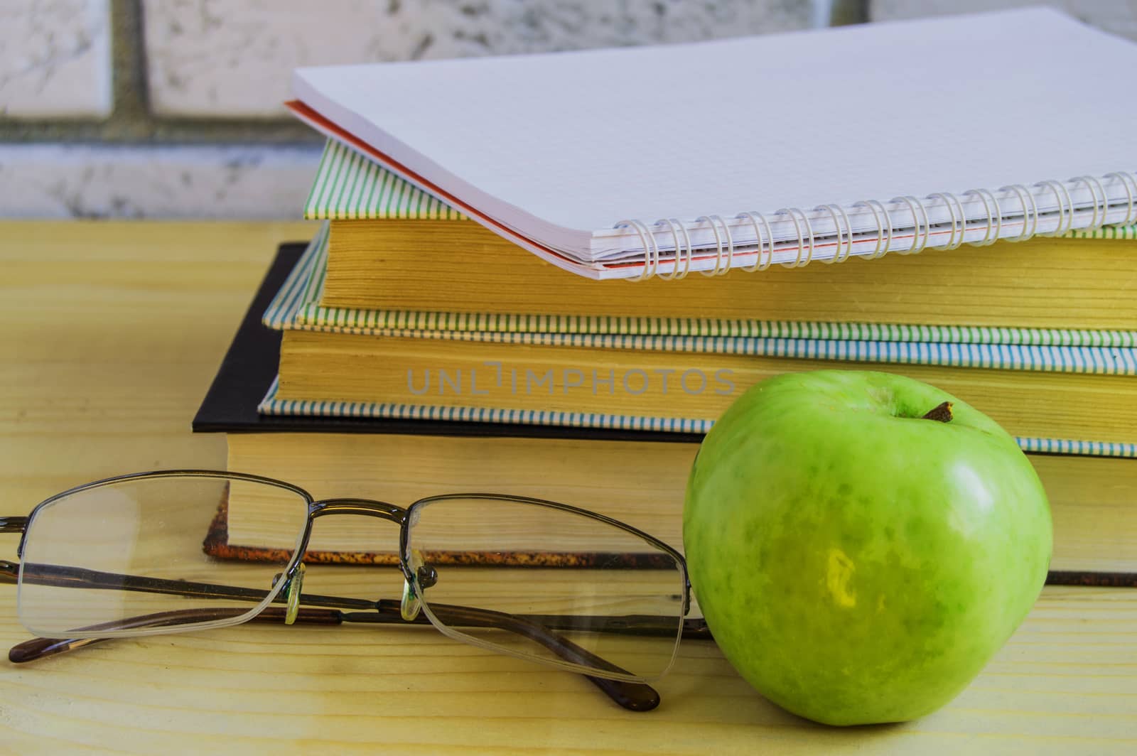 Teacher's Day concept and back to school, green Apple, book, laptop, reading glasses and pen on wooden table, sunlight by claire_lucia