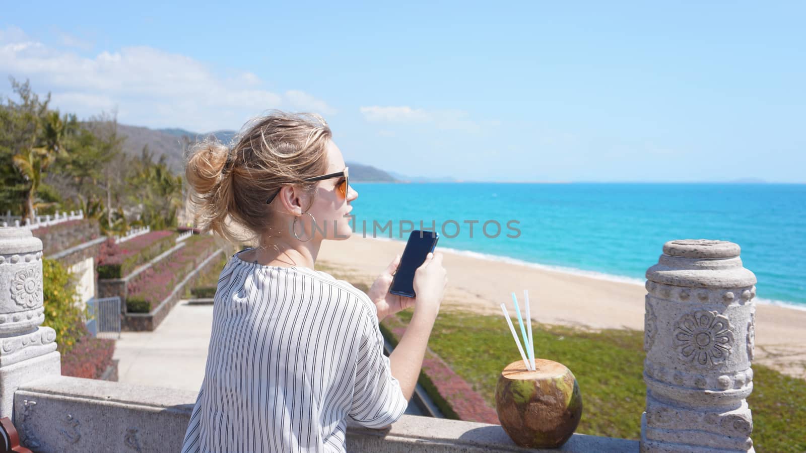A beautiful young woman on a tropical beach with a phone in her hands by natali_brill