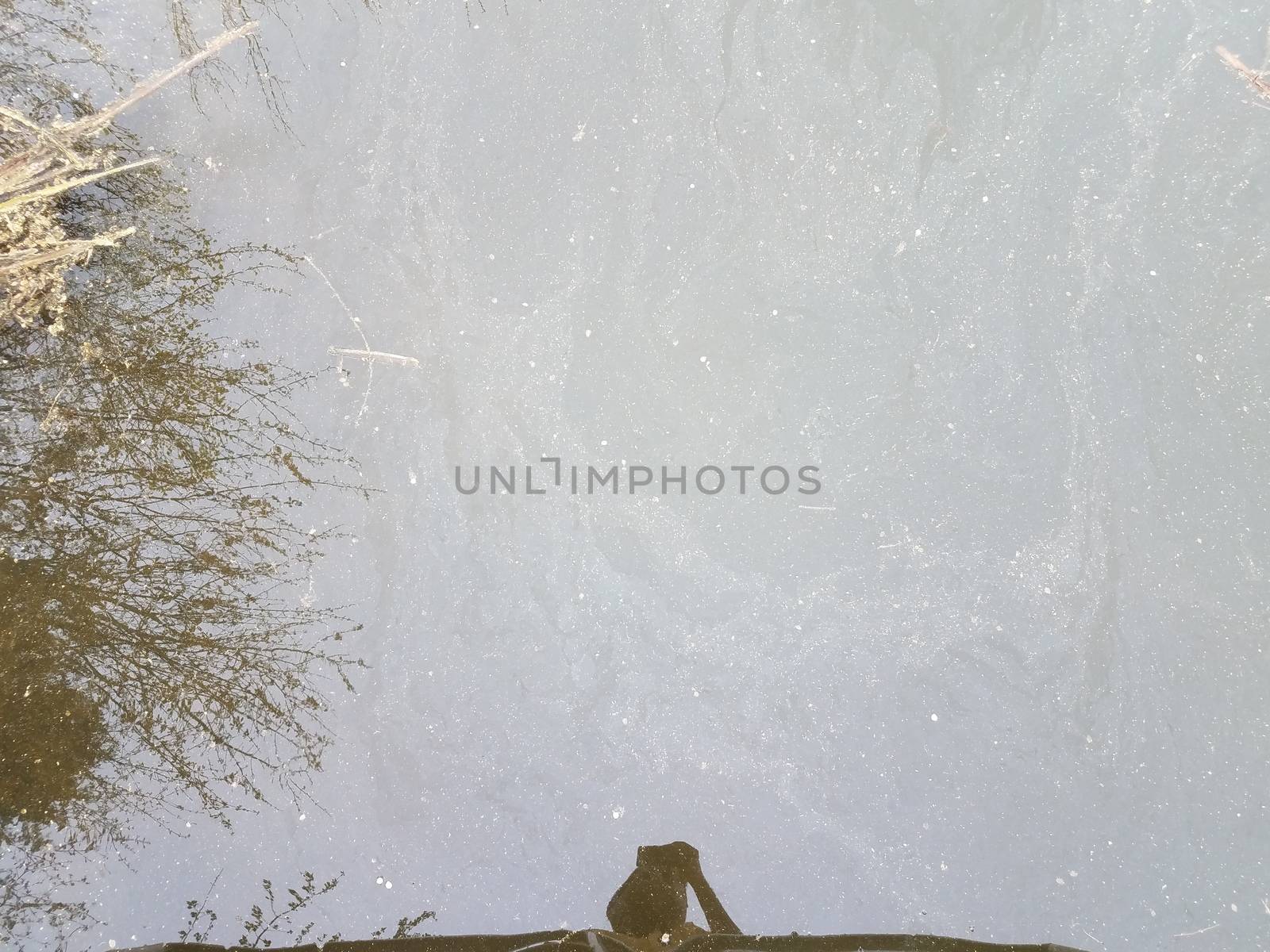 dirty or murky stagnant water with reflection of grasses and person by stockphotofan1