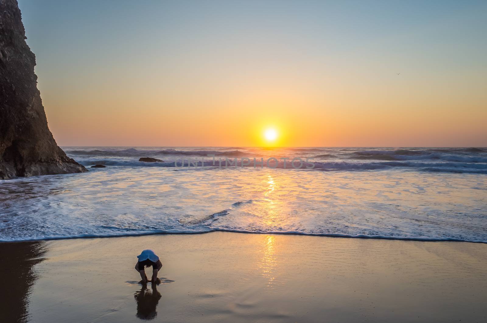 A little boy is playing with the sand at Praia da Adraga during sunset.