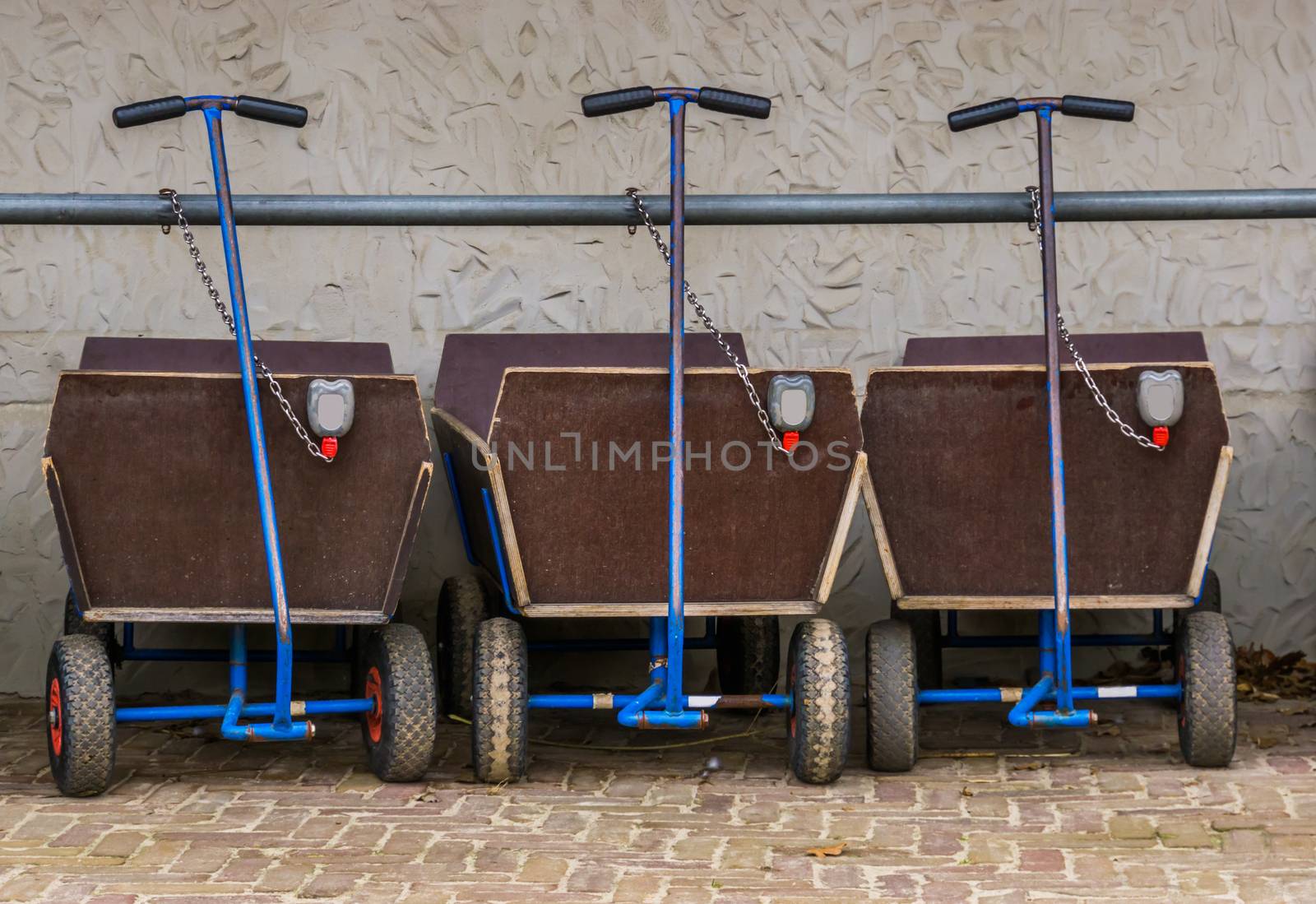 a row of pulling carts for baggage and children, locked and leashed on a metal bar, outdoor transportation