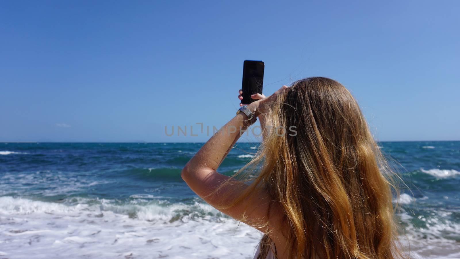 Closeup of a female using mobile phone, beach and sea on background. Women uses mobile app
