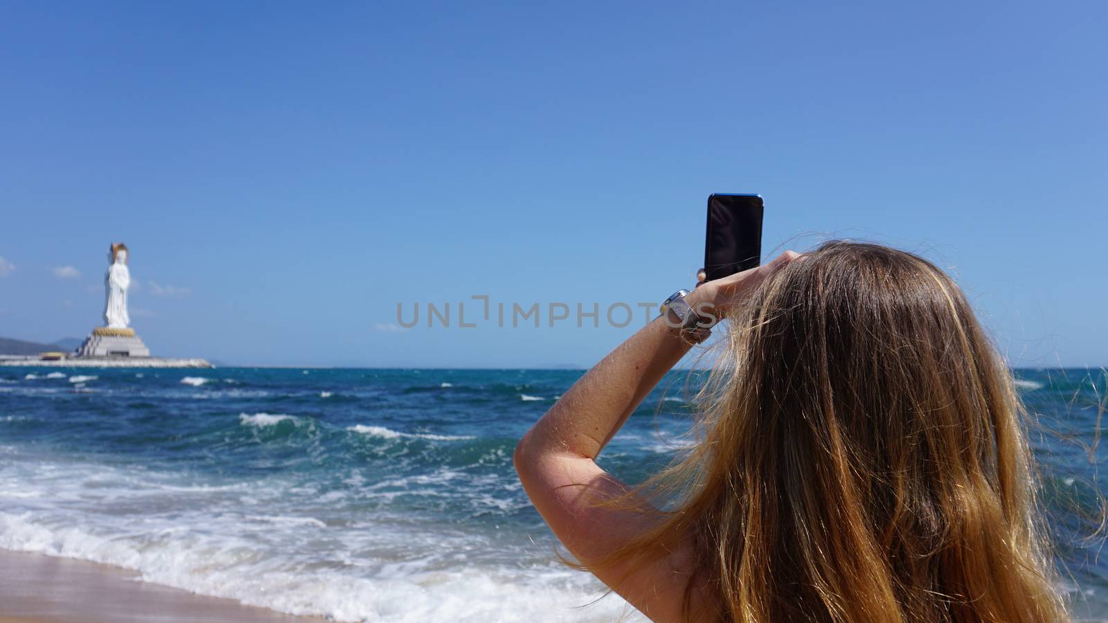 Closeup of a female using mobile phone, beach and sea on background by natali_brill