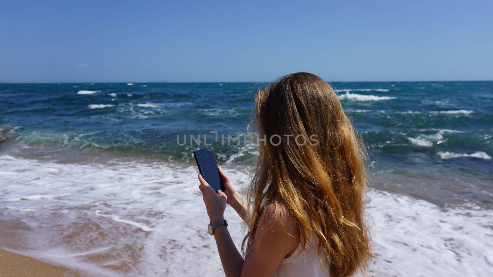 Closeup of a female using mobile phone, beach and sea on background. Women uses mobile app