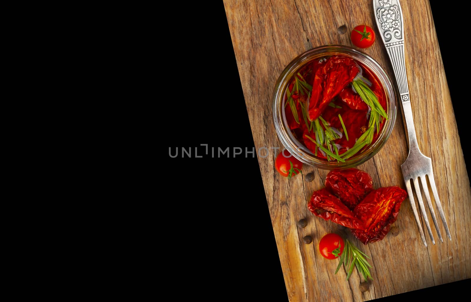 Delicious dried tomatoes in the jar of olive oil, the fork on wood background. In rustic style. With a space for text.