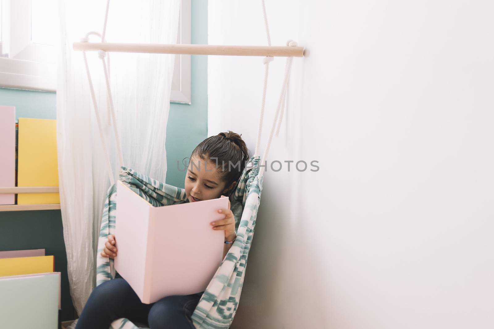 cute little kid girl is reading a book at home. funny lovely child having fun in kids room. copy space for text