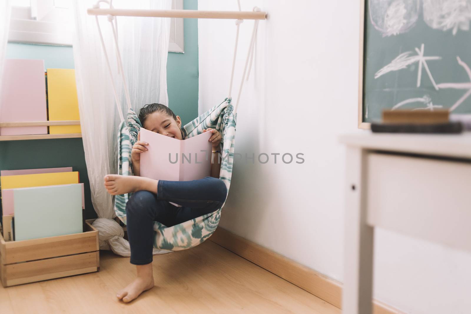 little girl having fun while reading a book in her kids room near the window, funny lovely child having fun at home, copy space for text