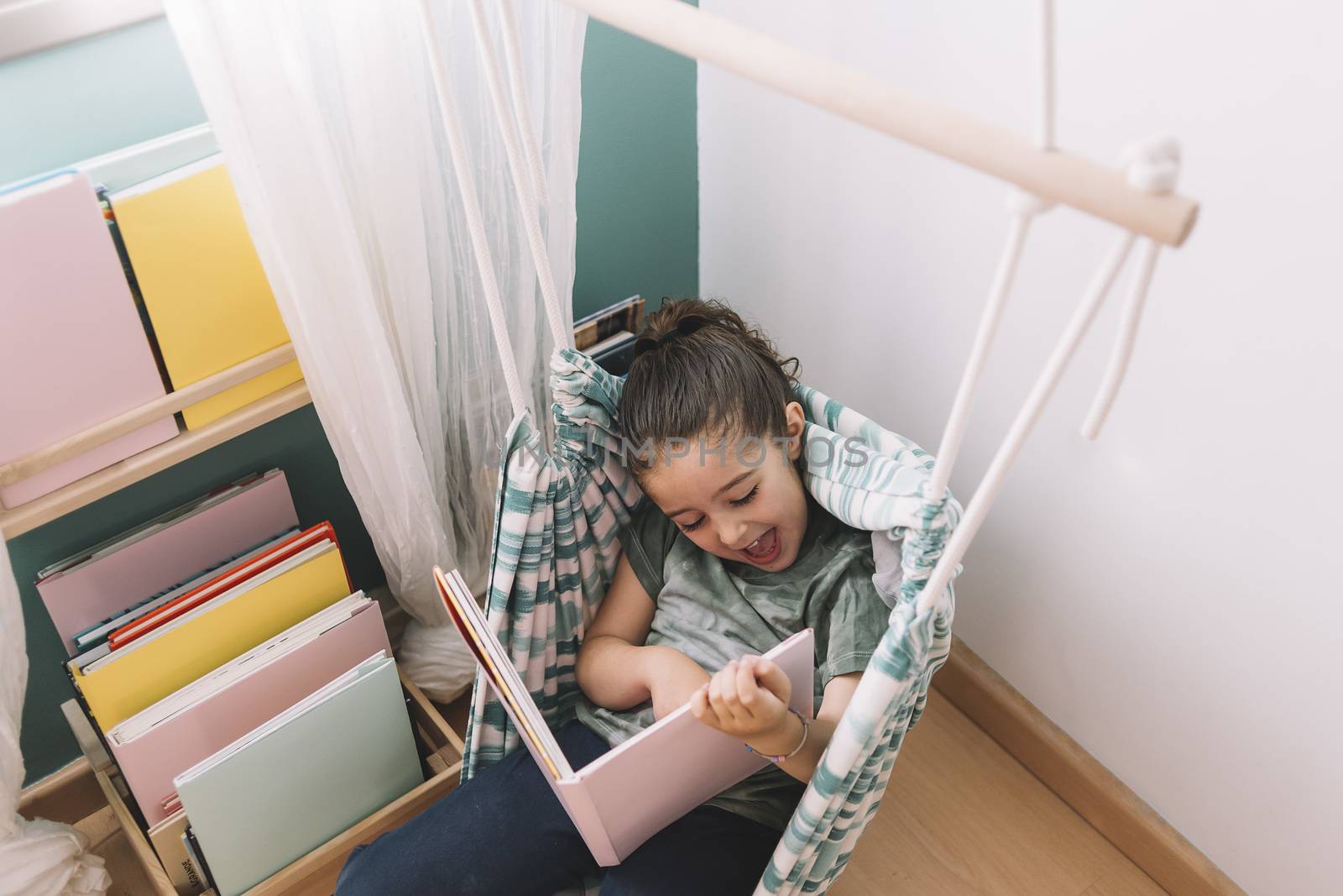 little girl laughing funny while reading a book at home near the window, funny lovely child having fun in her kids room, copy space for text