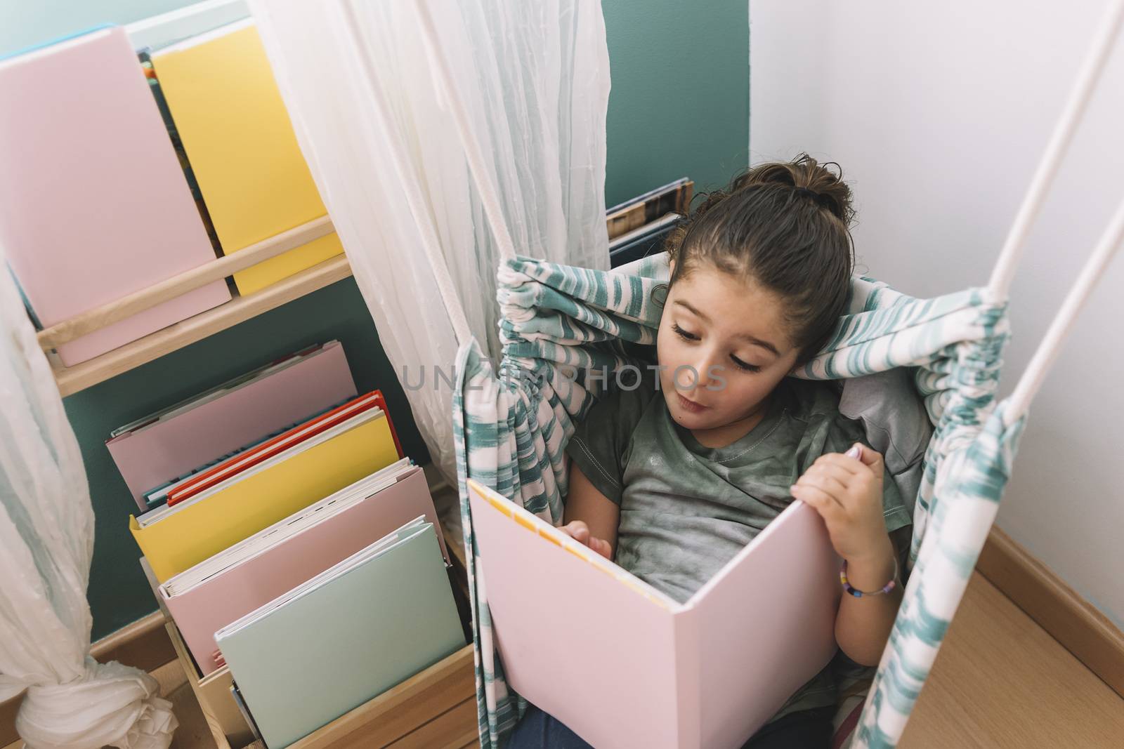 little girl surprised and excited reading a book at home near the window, funny lovely child having fun in her kids room, copy space for text