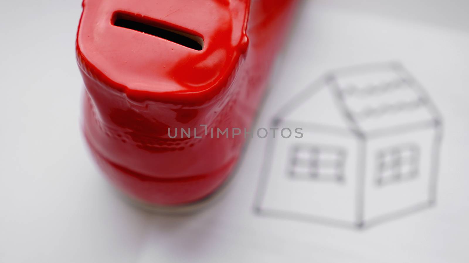 Hand dropping coin into the moneybox. Drawing a house on a white sheet near with a box