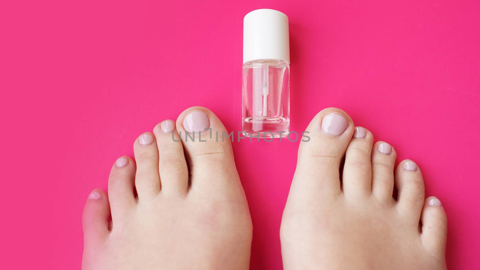 Pedicure with transparent nail polish on pink background. Healthy feet, health care