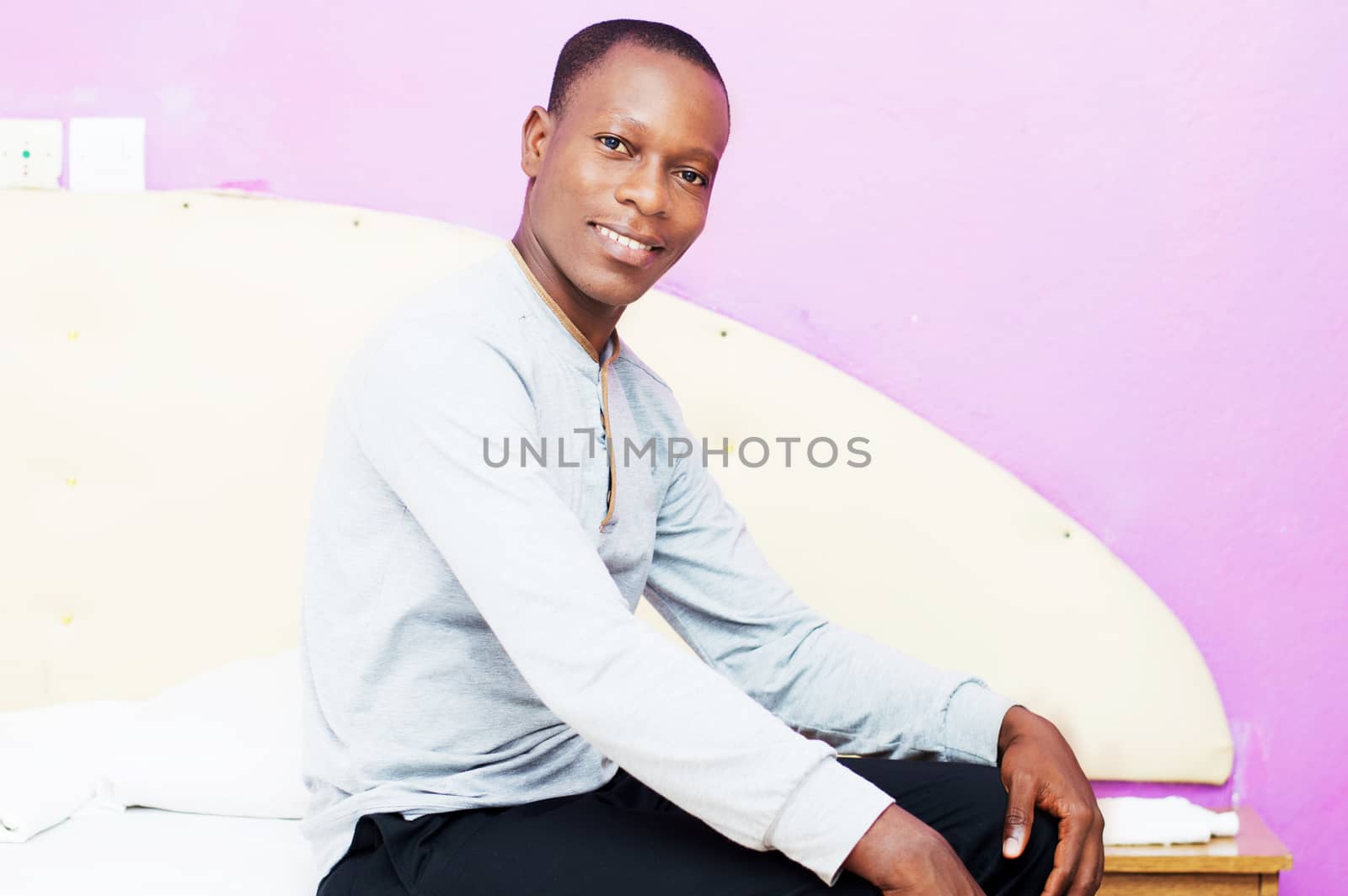 this young man dressed in the morning sitting on his bed cheerful face to the camera