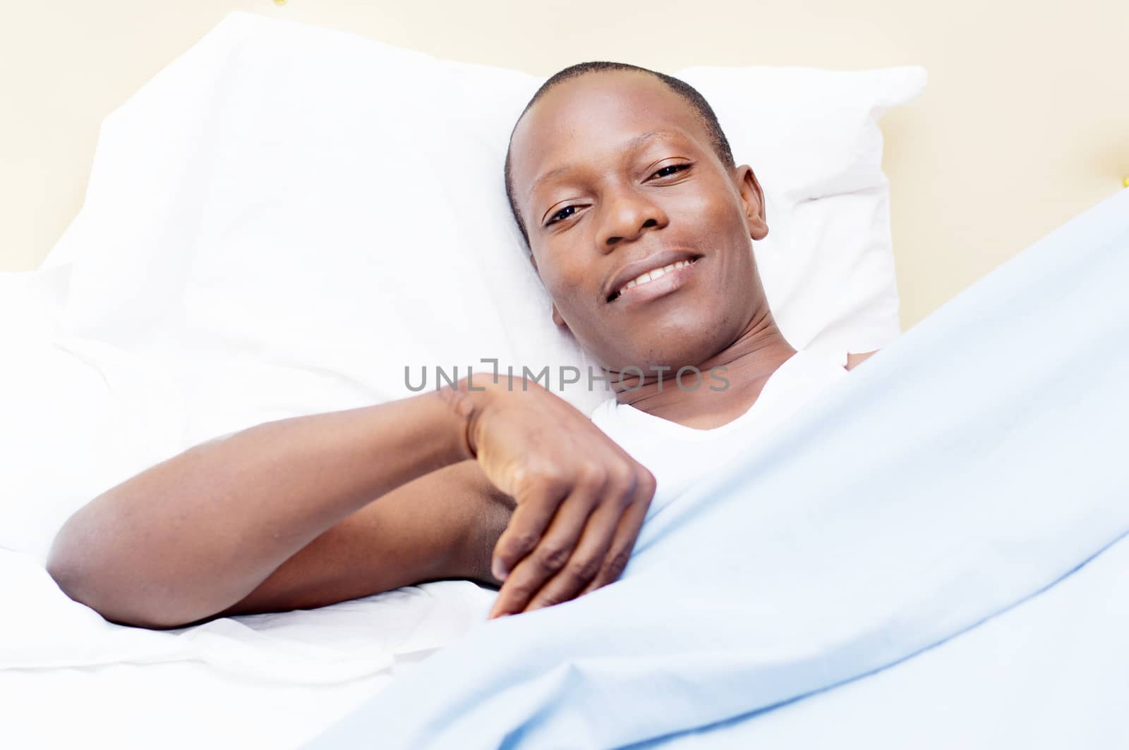 this young man lying on a bed, ready to cover smile at the camera.